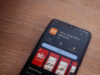 Lod, Israel - 16 Temmuz 2023: Temu app playstore page on smartphone on wood background. Üst görünüm düzlüğü kopyalama alanı ile yatıyordu.