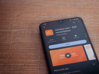 Lod, Israel - 16 Temmuz 2023: Alibaba.com uygulama oyun mağazası sayfası ahşap zemin üzerinde akıllı telefon. Üst görünüm düzlüğü kopyalama alanı ile yatıyordu.