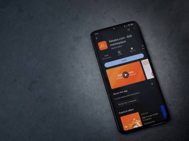 Lod, Israel - 16 Temmuz 2023: Alibaba.com uygulama oyun mağazası sayfası kara mermer taşlı arka planda akıllı telefon. Üst görünüm düzlüğü kopyalama alanı ile yatıyordu.