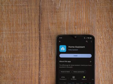 Lod, Israel - July 16,2023: Home Assistant app play store page on smartphone on wooden background. Top view flat lay with copy space.