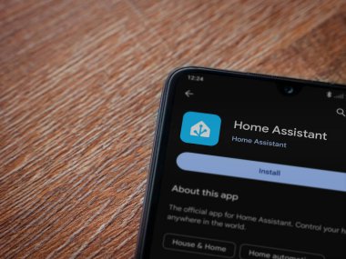 Lod, Israel - July 16,2023: Home Assistant app play store page on smartphone on wooden background. Top view flat lay with copy space.