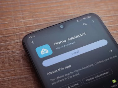 Lod, Israel - July 16,2023: Home Assistant app play store page on smartphone on wooden background. Top view flat lay with copy space.