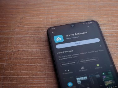 Lod, Israel - July 16,2023: Home Assistant app play store page on smartphone on wooden background. Top view flat lay with copy space.