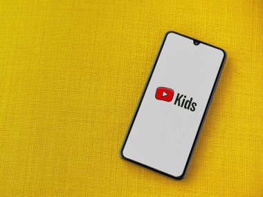 Lod, Israel - 16 Temmuz 2023: YouTube Kids uygulama ekranı sarı kumaş arka planda akıllı telefondan çalıştırıldı. Üst görünüm düzlüğü kopyalama alanı ile yatıyordu.