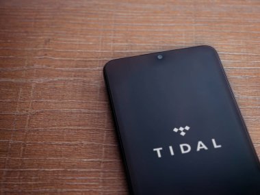 Lod, Israel - 16 Temmuz 2023: TIDAL Müzik uygulaması ahşap zemin üzerinde akıllı telefon fırlatma ekranı. Üst görünüm düzlüğü kopyalama alanı ile yatıyordu.