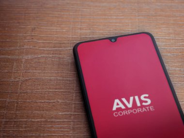 Lod, Israel - 16 Temmuz 2023: Avis Corporate uygulaması ahşap zemin üzerinde akıllı telefon fırlatma ekranı. Üst görünüm düzlüğü kopyalama alanı ile yatıyordu.