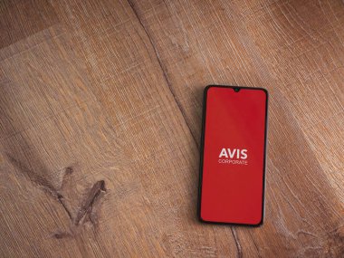 Lod, Israel - 16 Temmuz 2023: Avis Corporate uygulaması ahşap zemin üzerinde akıllı telefon fırlatma ekranı. Üst görünüm düzlüğü kopyalama alanı ile yatıyordu.