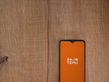 Lod, Israel - 16 Temmuz 2023: Ahşap arka planda akıllı telefondan Temu uygulama başlatma ekranı. Üst görünüm düzlüğü kopyalama alanı ile yatıyordu.