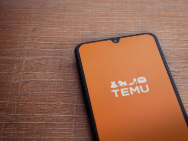 Lod, Israel - 16 Temmuz 2023: Ahşap arka planda akıllı telefondan Temu uygulama başlatma ekranı. Üst görünüm düzlüğü kopyalama alanı ile yatıyordu.
