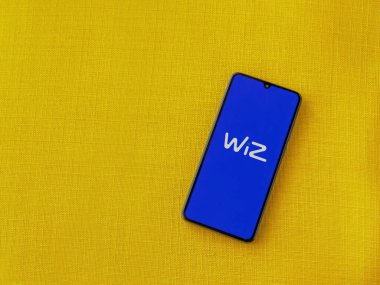 Lod, Israel - 16 Temmuz 2023: WIZ uygulama ekranı sarı kumaş arka planda akıllı telefon. Üst görünüm düzlüğü kopyalama alanı ile yatıyordu.