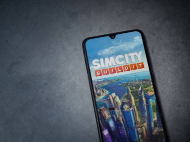 Lod, Israel - 16 Temmuz 2023: SimCity BuildIt uygulaması koyu mermer taşlı arka planda akıllı telefondan kalkış ekranı. Üst görünüm düzlüğü kopyalama alanı ile yatıyordu.