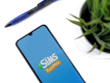 Lod, Israel - 16 Temmuz 2023: Beyaz arka planda The Sims FreePlay uygulamalı akıllı telefonlu modern çalışma alanı. Üst görünüm yatağını kapat.