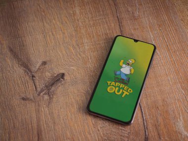 Lod, Israel - 16 Temmuz 2023: Simpsonlar ahşap arka planda akıllı telefondan uygulama başlatma ekranını kapattılar. Üst görünüm düzlüğü kopyalama alanı ile yatıyordu.