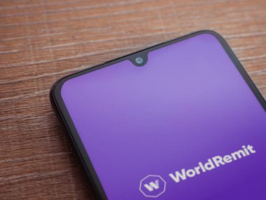 Lod, Israel - 16 Temmuz 2023: WorldRemit uygulaması ahşap arka planda akıllı telefondan çalıştırma ekranı. Üst görünüm düzlüğü kopyalama alanı ile yatıyordu.