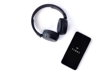 Lod, Israel - 16 Temmuz 2023: TIDAL Müzik uygulamalı akıllı telefon fırlatma ekranı ve beyaz arka planda kablosuz kulaklıklar. Üst görünüm düzlüğü kopyalama alanı ile yatıyordu.