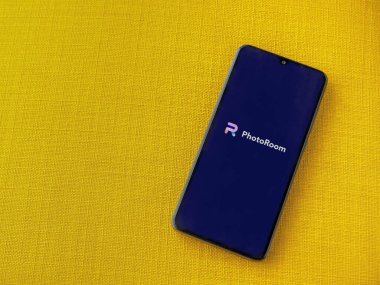 Lod, Israel - 16 Temmuz 2023: Fotoğraf Odası Stüdyosu Fotoğraf Editörü uygulama ekranı sarı kumaş arka planda akıllı telefonu çalıştırıyor. Üst görünüm düzlüğü kopyalama alanı ile yatıyordu.