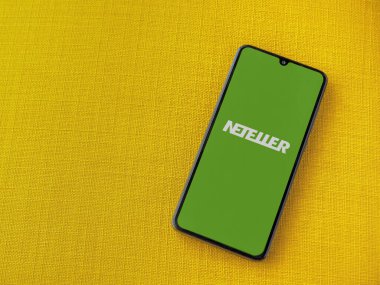 Lod, Israel - 16 Temmuz 2023: NETELLER uygulama ekranı sarı kumaş arka planda akıllı telefondan çalıştırılıyor. Üst görünüm düzlüğü kopyalama alanı ile yatıyordu.
