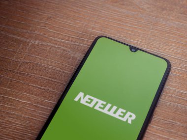 Lod, Israel - 16 Temmuz 2023: NETELLER uygulama ekranı ahşap zemin üzerinde akıllı telefon. Üst görünüm düzlüğü kopyalama alanı ile yatıyordu.