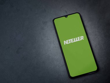 Lod, Israel - 16 Temmuz 2023: NETELLER uygulaması koyu mermer taşlı arka planda akıllı telefondan kalkış ekranı. Üst görünüm düzlüğü kopyalama alanı ile yatıyordu.