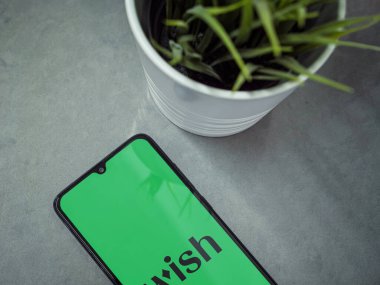 Lod, Israel - 16 Temmuz 2023: Dilek uygulamasının mermer zemin üzerinde başlatıldığı akıllı telefonlu modern çalışma alanı. Üst görünüm yatağını kapat.