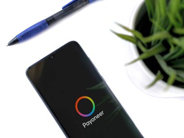 Lod, Israel - 16 Temmuz 2023: Beyaz zemin üzerinde Payoneer uygulaması olan akıllı telefonlu modern çalışma alanı. Üst görünüm yatağını kapat.