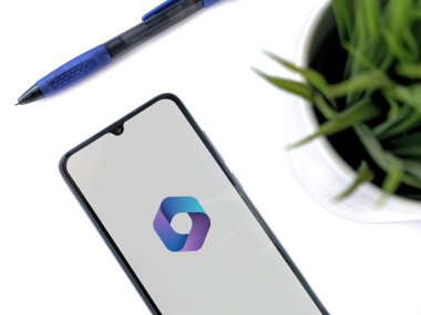 Lod, Israel - 16 Temmuz 2023: Beyaz arka planda Microsoft 360 uygulamalı akıllı telefonlu modern çalışma alanı. Üst görünüm yatağını kapat.