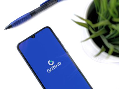 Lod, Israel - 16 Temmuz 2023: Beyaz zemin üzerinde Gate.io uygulaması olan akıllı telefonlu modern çalışma alanı. Üst görünüm yatağını kapat.