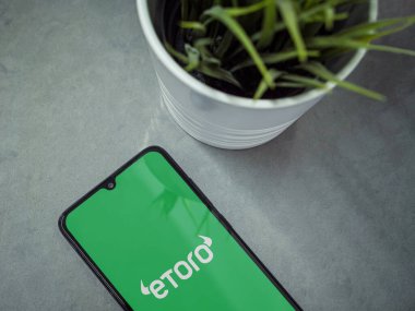 Lod, Israel - 16 Temmuz 2023: eToro uygulamalı akıllı telefonlu modern çalışma alanı mermer zemin üzerinde fırlatma ekranı. Üst görünüm yatağını kapat.