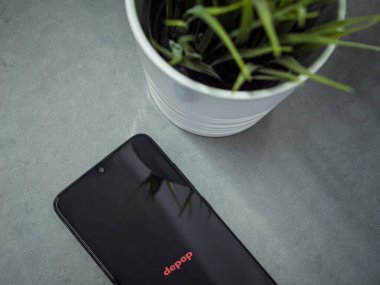 Lod, Israel - 16 Temmuz 2023: Mermer zemin üzerinde Depop uygulaması fırlatma ekranı olan akıllı telefonlu modern çalışma alanı. Üst görünüm yatağını kapat.