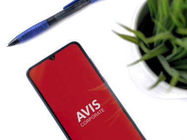 Lod, Israel - 16 Temmuz 2023: Beyaz zemin üzerinde Avis Corporate uygulaması olan akıllı telefonlu modern çalışma alanı. Üst görünüm yatağını kapat.