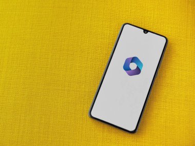 Lod, Israel - 16 Temmuz 2023: Microsoft 360 uygulama ekranı sarı kumaş arka planda akıllı telefon. Üst görünüm düzlüğü kopyalama alanı ile yatıyordu.