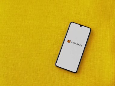 Lod, Israel - 16 Temmuz 2023: MetaMaske uygulaması sarı kumaş arka planda akıllı telefondan çalıştırma ekranı. Üst görünüm düzlüğü kopyalama alanı ile yatıyordu.