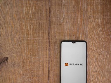 Lod, Israel - 16 Temmuz 2023: MetaMaske uygulaması ahşap arka planda akıllı telefondan çalıştırma ekranı. Üst görünüm düzlüğü kopyalama alanı ile yatıyordu.