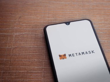 Lod, Israel - 16 Temmuz 2023: MetaMaske uygulaması ahşap arka planda akıllı telefondan çalıştırma ekranı. Üst görünüm düzlüğü kopyalama alanı ile yatıyordu.