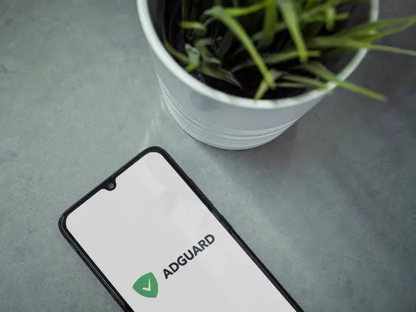 stock image Lod, Israel - July 16,2023: Modern workspace with smartphone with AdGuard app launch screen on marble background. Close up top view flat lay.