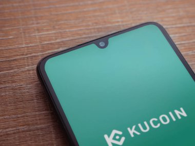 Lod, Israel - 16 Temmuz 2023: KuCoin uygulama ekranı ahşap arka planda akıllı telefon. Üst görünüm düzlüğü kopyalama alanı ile yatıyordu.