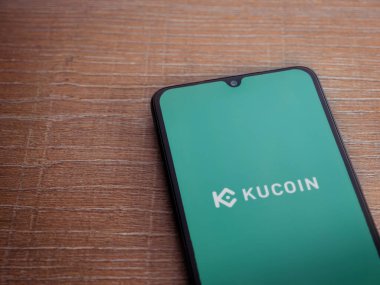 Lod, Israel - 16 Temmuz 2023: KuCoin uygulama ekranı ahşap arka planda akıllı telefon. Üst görünüm düzlüğü kopyalama alanı ile yatıyordu.
