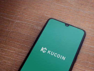 Lod, Israel - 16 Temmuz 2023: KuCoin uygulama ekranı ahşap arka planda akıllı telefon. Üst görünüm düzlüğü kopyalama alanı ile yatıyordu.