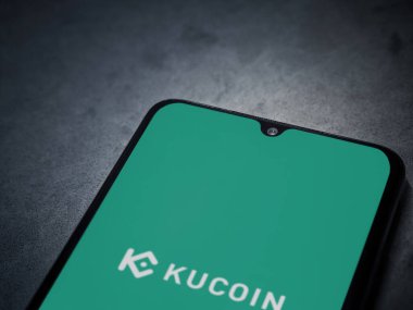 Lod, Israel - 16 Temmuz 2023: KuCoin uygulaması koyu mermer taşlı arka planda akıllı telefondan kalkış ekranı. Üst görünüm düzlüğü kopyalama alanı ile yatıyordu.