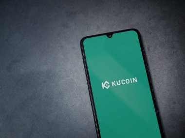 Lod, Israel - 16 Temmuz 2023: KuCoin uygulaması koyu mermer taşlı arka planda akıllı telefondan kalkış ekranı. Üst görünüm düzlüğü kopyalama alanı ile yatıyordu.
