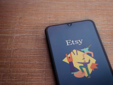 Lod, Israel - 16 Temmuz 2023: Etsy Seller uygulama ekranı ahşap arka planda akıllı telefon. Üst görünüm düzlüğü kopyalama alanı ile yatıyordu.