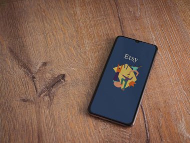Lod, Israel - 16 Temmuz 2023: Etsy Seller uygulama ekranı ahşap arka planda akıllı telefon. Üst görünüm düzlüğü kopyalama alanı ile yatıyordu.
