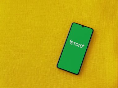 Lod, Israel - 16 Temmuz 2023: eToro uygulama ekranı sarı kumaş arka planda akıllı telefon. Üst görünüm düzlüğü kopyalama alanı ile yatıyordu.