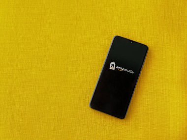 Lod, Israel - 16 Temmuz 2023: Amazon Seller uygulama ekranı sarı kumaş arka planda akıllı telefon. Üst görünüm düzlüğü kopyalama alanı ile yatıyordu.