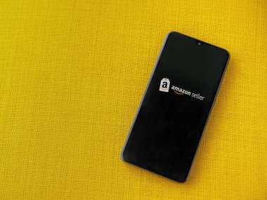 Lod, Israel - 16 Temmuz 2023: Amazon Seller uygulama ekranı sarı kumaş arka planda akıllı telefon. Üst görünüm düzlüğü kopyalama alanı ile yatıyordu.