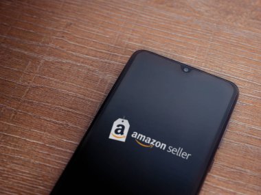 Lod, Israel - 16 Temmuz 2023: Amazon Seller uygulama ekranı ahşap arka planda akıllı telefondan çalıştırılıyor. Üst görünüm düzlüğü kopyalama alanı ile yatıyordu.