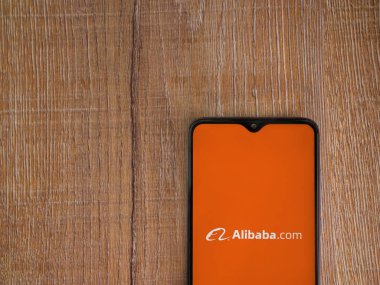 Lod, Israel - 16 Temmuz 2023: Alibaba.com uygulama ekranı ahşap arka planda akıllı telefon. Üst görünüm düzlüğü kopyalama alanı ile yatıyordu.