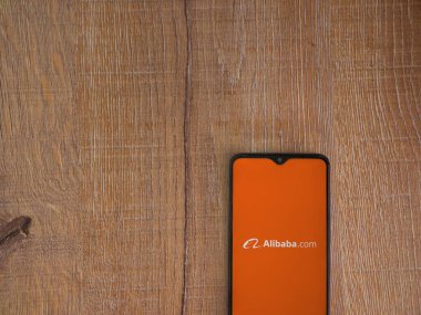 Lod, Israel - 16 Temmuz 2023: Alibaba.com uygulama ekranı ahşap arka planda akıllı telefon. Üst görünüm düzlüğü kopyalama alanı ile yatıyordu.