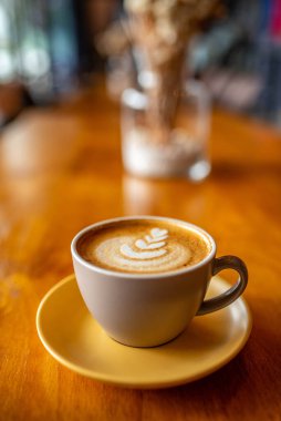 Tahta masada köpüklü bir fincan latte sanat kahvesi.