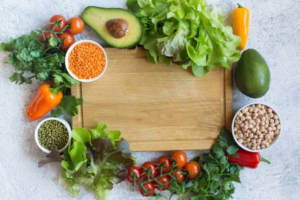 A wooden board with a variety of vegetables and grains, tomatoes, avocado, sweet pepper, salad leaves, and herbs. The grains include lentils, chickpeas, and beans to add complexity to a healthy meal.